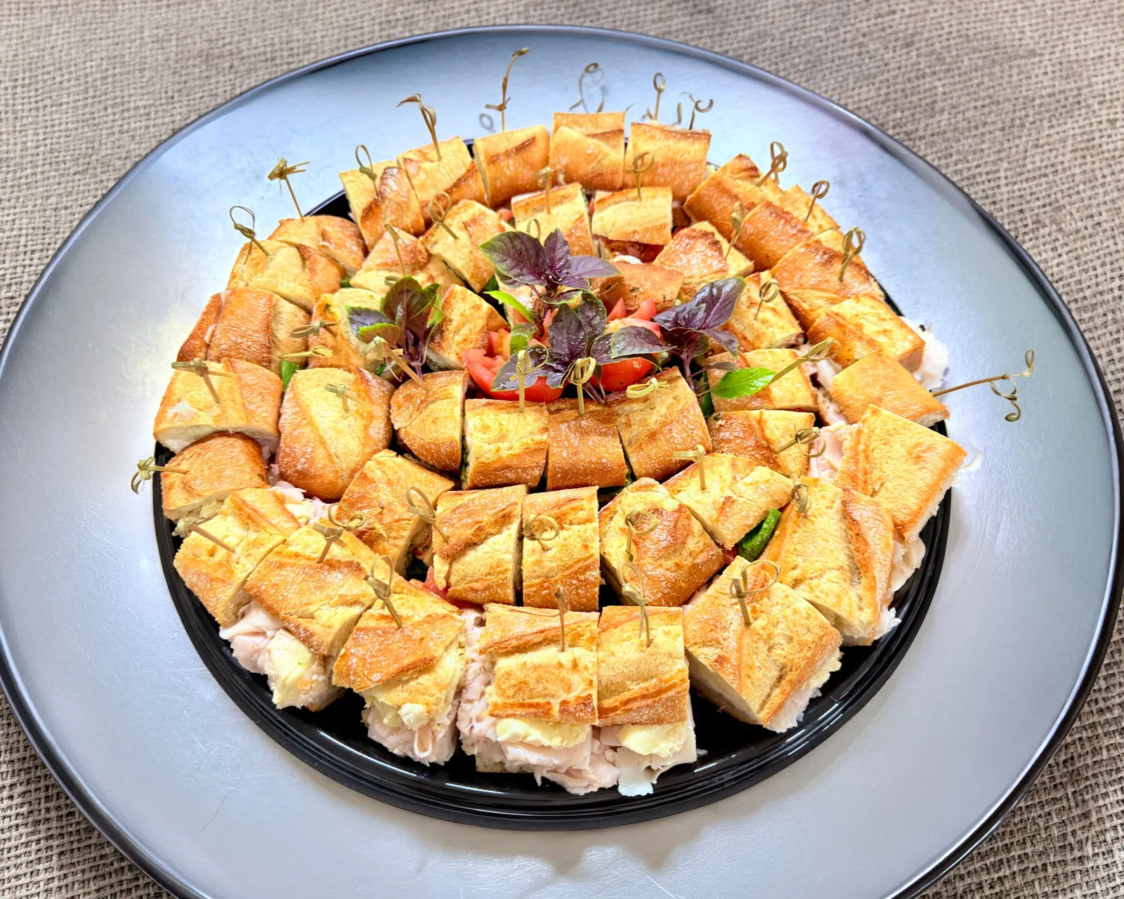 Spiral-arranged mini sandwiches on a round platter with herb garnish
